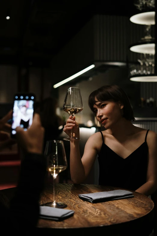 a woman sitting at a table holding a glass of wine, captured on iphone, nightcap, gemma chen, multiple stories