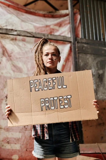 a woman holding a cardboard sign that says peaceful protest, an album cover, pexels contest winner, dreadlocks, leon tukker, thumbnail, teenage girl