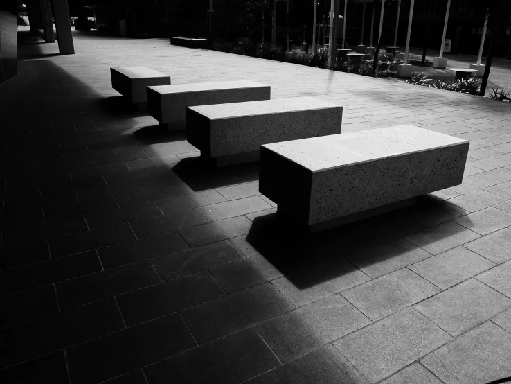 a black and white photo of a row of benches, inspired by Peter Basch, unsplash, concrete art, square shapes, dark warm light, three, polished concrete