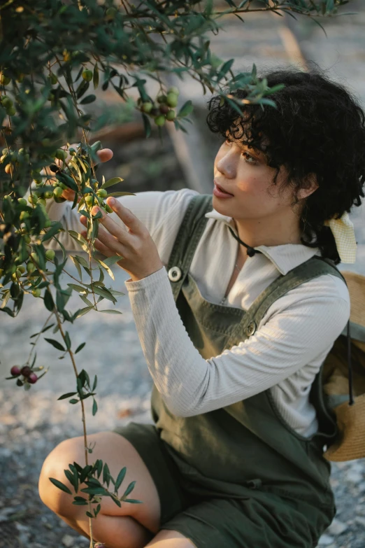 a woman sitting on the ground next to a tree, inspired by Jules Bastien-Lepage, trending on pexels, renaissance, wearing overalls, with fruit trees, finn wolfhard, pictured from the shoulders up