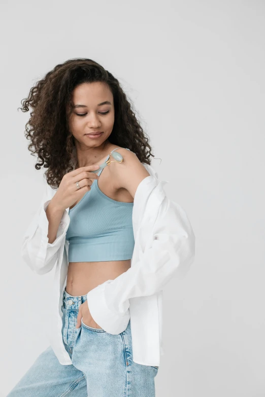 a beautiful young woman in a blue top and jeans posing on a white background, by Gavin Hamilton, trending on pexels, process art, with an iv drip, wearing : tanktop, earbuds jewelry, white coat