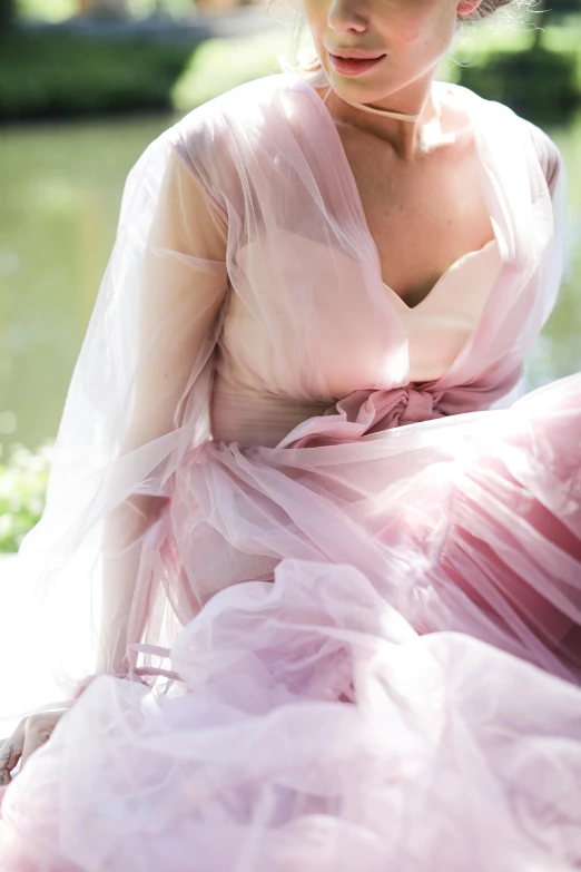 a woman in a pink dress sitting next to a body of water, wearing organza gown, up close, soft colours, lavender blush