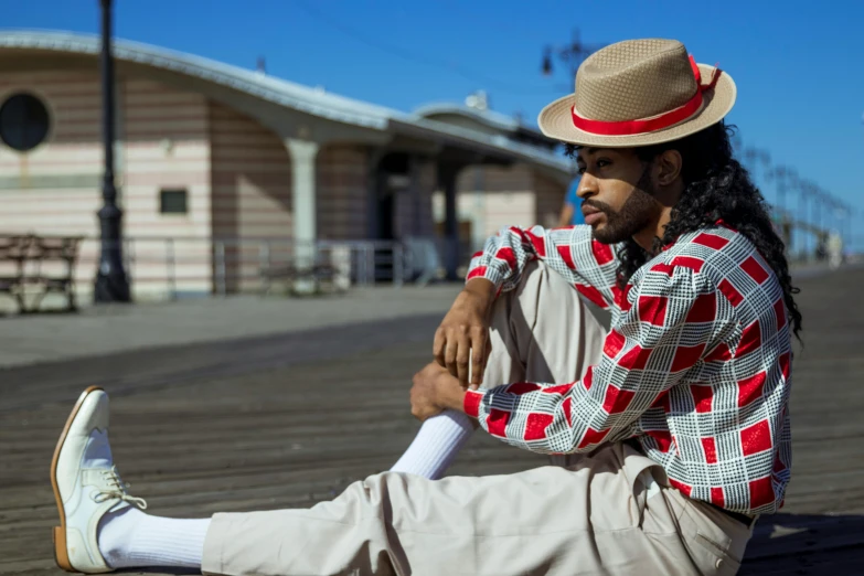 a man sitting on a boardwalk wearing a hat, inspired by Ismail Gulgee, wearing rr diner uniform, red suit, wearing off - white style, patterns