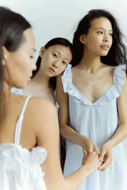 a group of women standing in front of a mirror, inspired by Vanessa Beecroft, trending on pexels, renaissance, wearing a nightgown, young asian girl, thoughtful expression, white and pale blue