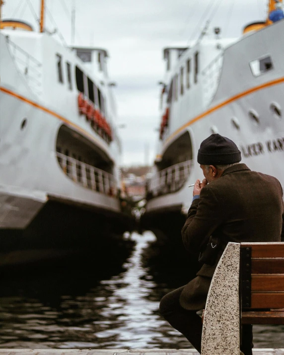 a man sitting on a bench in front of two boats, pexels contest winner, happening, lgbtq, water surrounds the ship, the thinker, enes dirig