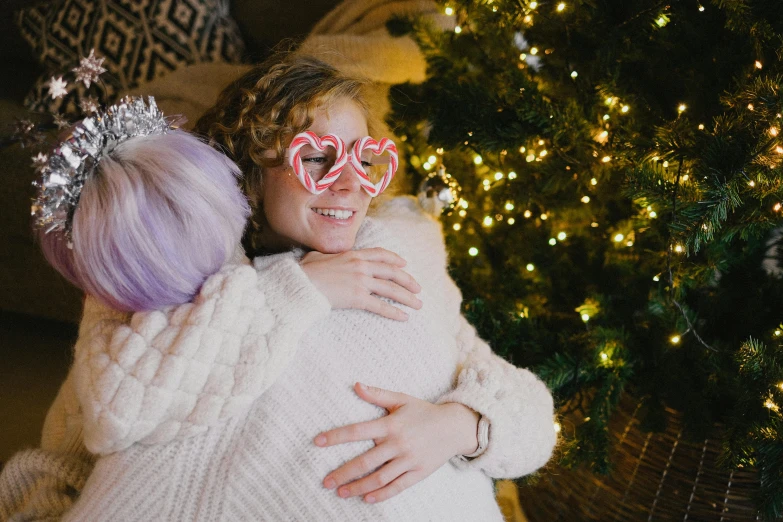 two girls hugging each other in front of a christmas tree, pexels, woman with rose tinted glasses, gif, plushie photography, abcdefghijklmnopqrstuvwxyz