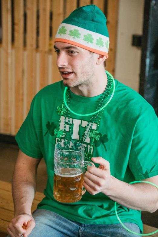 a man sitting on a bench holding a glass of beer, green hat, kyle hotz, irish, wearing fitness gear