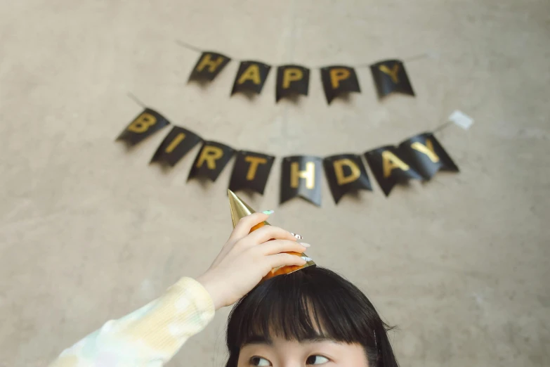 a little girl standing in front of a happy birthday banner, by Julia Pishtar, trending on unsplash, black and gold colors, ulzzang, 🍸🍋, greeting hand on head