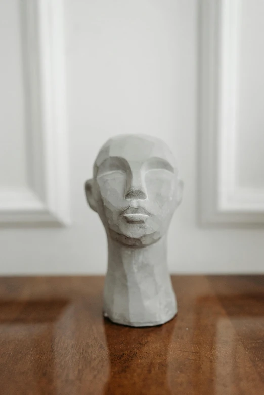 a white sculpture sitting on top of a wooden table, beautiful smooth oval head, made of cement, hestiasula head, full round face!