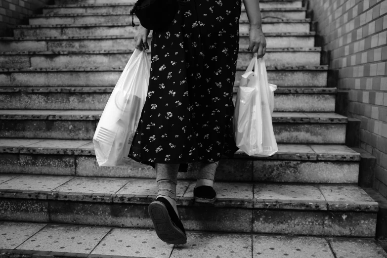 a black and white photo of a woman walking up some stairs, getting groceries, garbage plastic, long dress female, identical picture