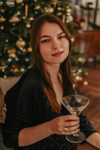 a woman holding a wine glass in front of a christmas tree, a portrait, by Julia Pishtar, pexels, around 20 yo, holding a martini, gif, anna nikonova aka newmilky