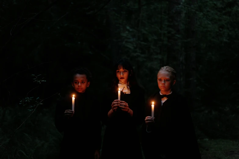 a group of people holding candles in the dark, inspired by Vanessa Beecroft, hansel and gretel, three women, wearing black robes, political meeting in the woods