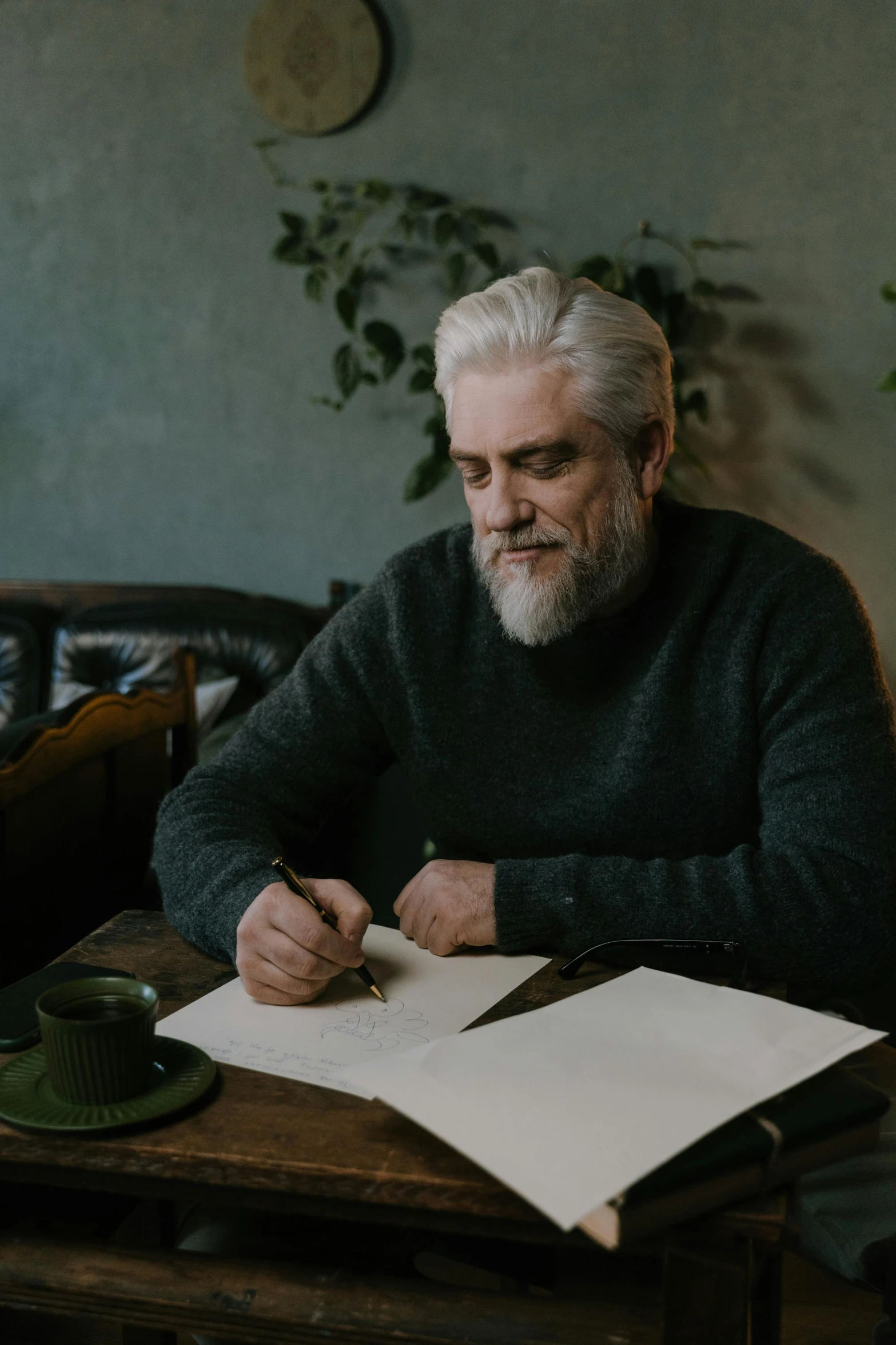 a man sitting at a table writing on a piece of paper, by Oskar Lüthy, pexels contest winner, realism, silver hair and beard, william dafoe, promotional image, middle - age