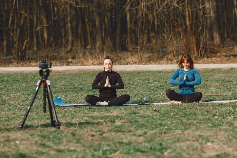 a couple of women sitting on top of a grass covered field, unsplash, video art, yoga, lunging at camera :4, avatar image, camera photo