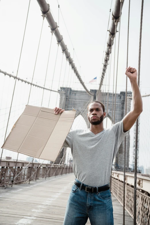 a man standing on a bridge holding a box, pexels contest winner, black arts movement, attacking nyc, brown paper, standing triumphant and proud, lean man with light tan skin