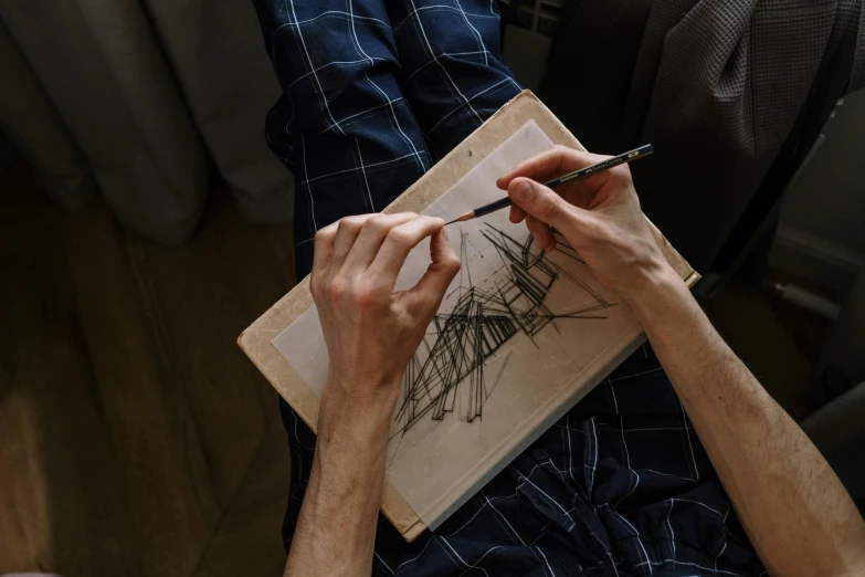 a man is drawing on a piece of paper, a drawing, by Jakub Husnik, pexels contest winner, visual art, holding a book, crosshatch, a high angle shot, inspired in balthus