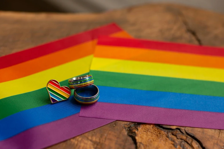 a couple of rings sitting on top of a piece of paper, inspired by Okuda Gensō, unsplash, lgbt flag, on a wooden desk, solid colours material, medium close up shot