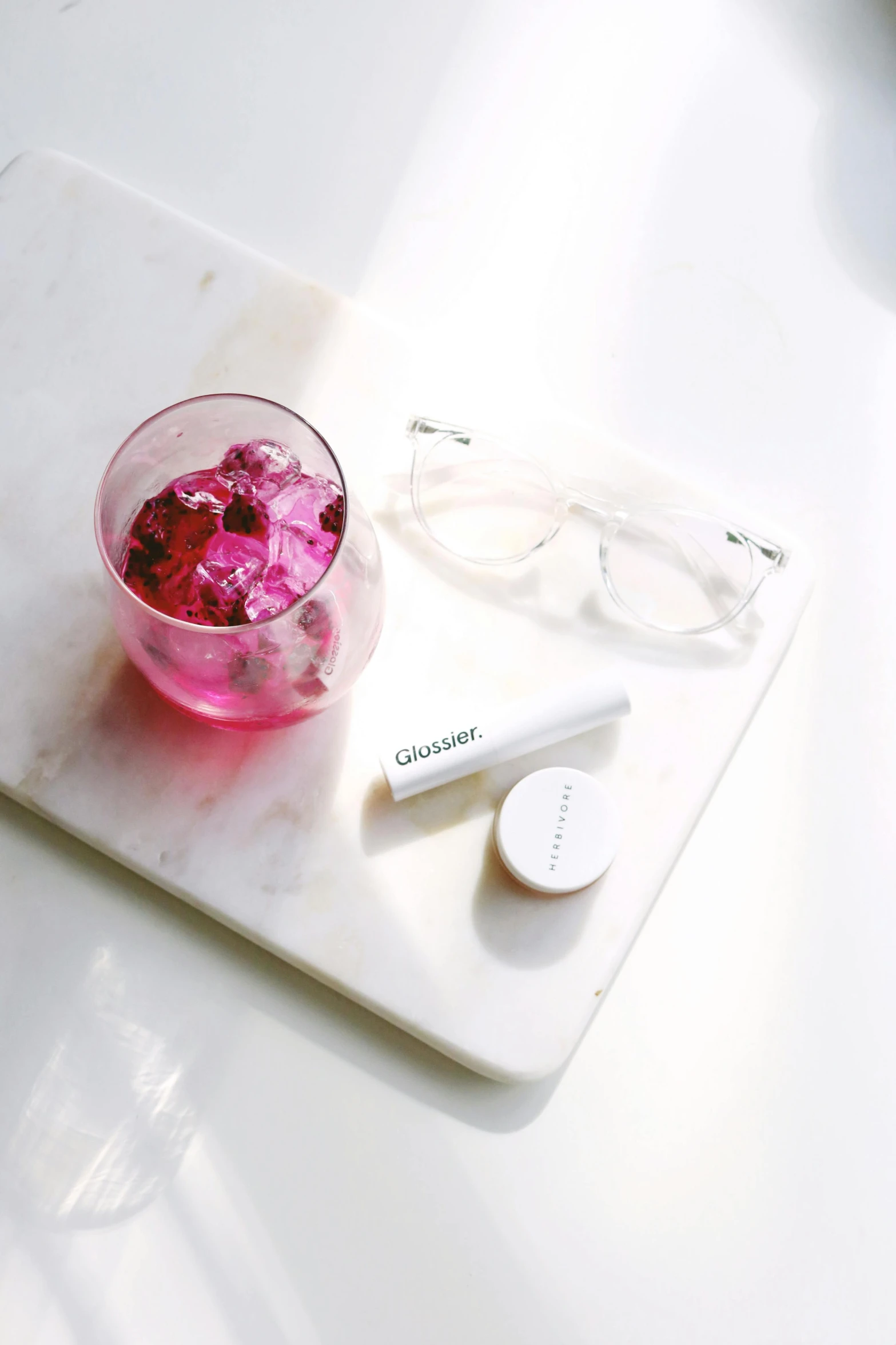 a glass of pink liquid sitting on top of a cutting board, inspired by An Gyeon, rounded eyeglasses, pills, sleek white, while marble