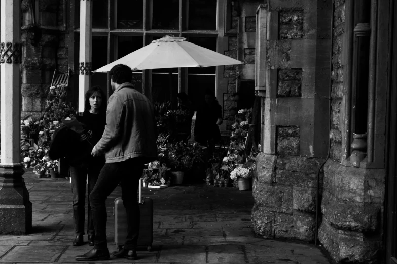 a man and a woman standing under an umbrella, a black and white photo, by John Hutton, pexels, flower shop scene, on a dark winter's day, in a square, waiting