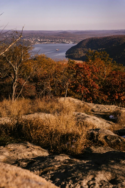 a man standing on top of a rock next to a lake, a picture, unsplash contest winner, hudson river school, autumn overgrowth, panorama distant view, 1990s photograph, cityscape