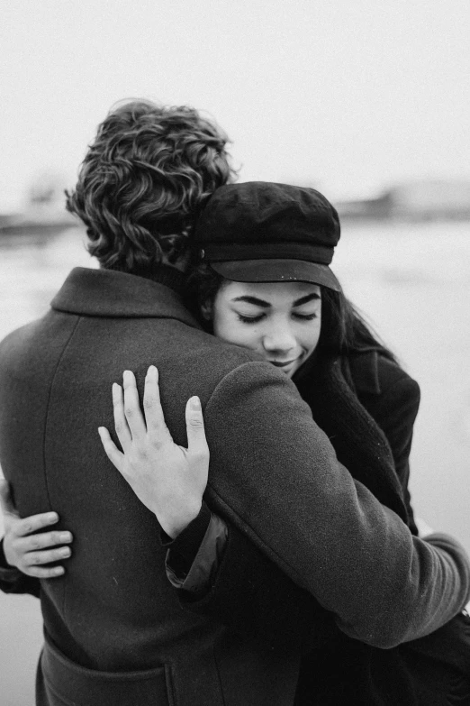 a man hugging a woman on the beach, a black and white photo, by Lucia Peka, pexels, an oversized beret, handsome girl, 😭 🤧 💔, romantic couple