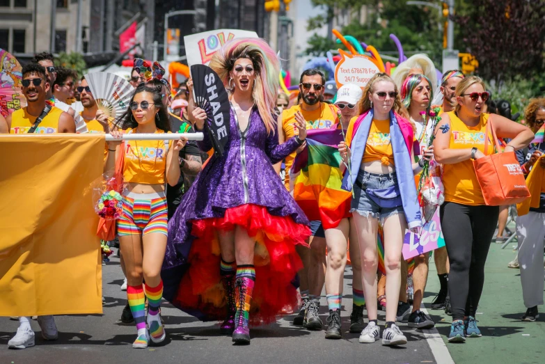 a group of women walking down a street holding flags, a cartoon, pexels, renaissance, rainbow tubing, orange and yellow costume, sydney hanson, in front of a large crowd