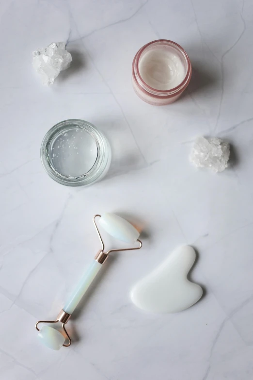 a couple of rollers sitting on top of a table, by Jessie Algie, trending on pexels, skin care, spoon placed, white marble, opal