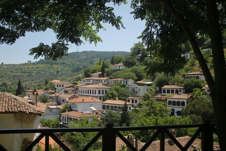 a view of a town from the top of a hill, white buildings with red roofs, akitipe studios, avalon, with dark trees in foreground