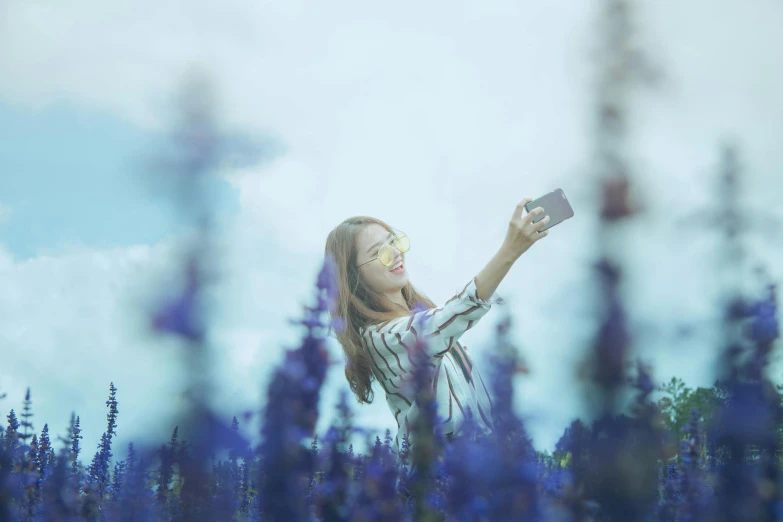 a woman taking a picture in a field of flowers, pexels contest winner, blue and violet, hold up smartphone, avatar image, color film photography