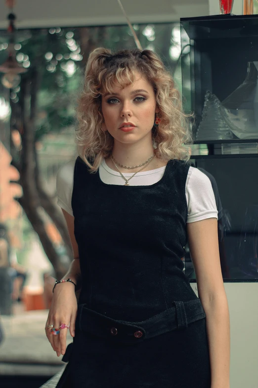 a woman in a black dress posing for a picture, an album cover, inspired by Nan Goldin, trending on pexels, short curly blonde haired girl, overalls, sydney sweeney, in sao paulo