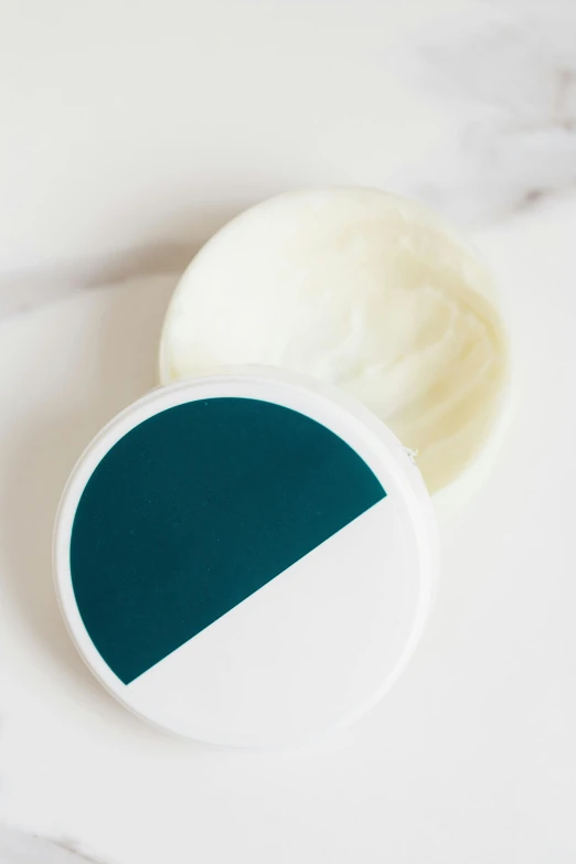 a jar of cream sitting on top of a marble counter, inspired by Eero Snellman, dark teal, split in half, on textured disc base, silicone skin