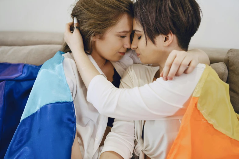 a couple sitting on top of a couch next to each other, by Arabella Rankin, trending on pexels, romanticism, lgbt flag, embrace, huang yuxing and aya takano, rainbow clothes