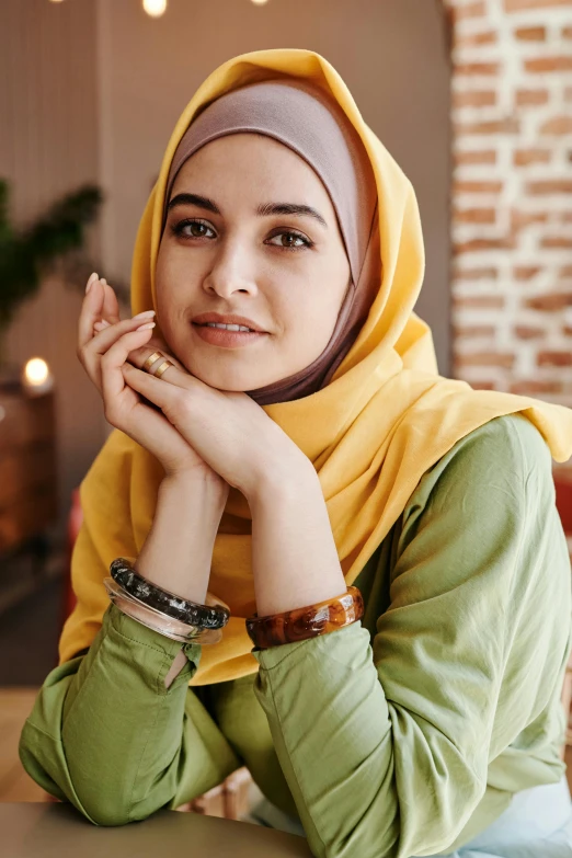 a woman wearing a hijab sitting at a table, lime and gold hue, wearing casual clothing, confident, h 9 6 0