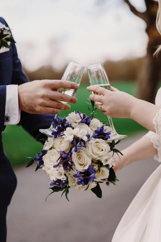 a man and a woman holding wine glasses, blue flowers accents, bouquet, sparkling spirits, exterior shot