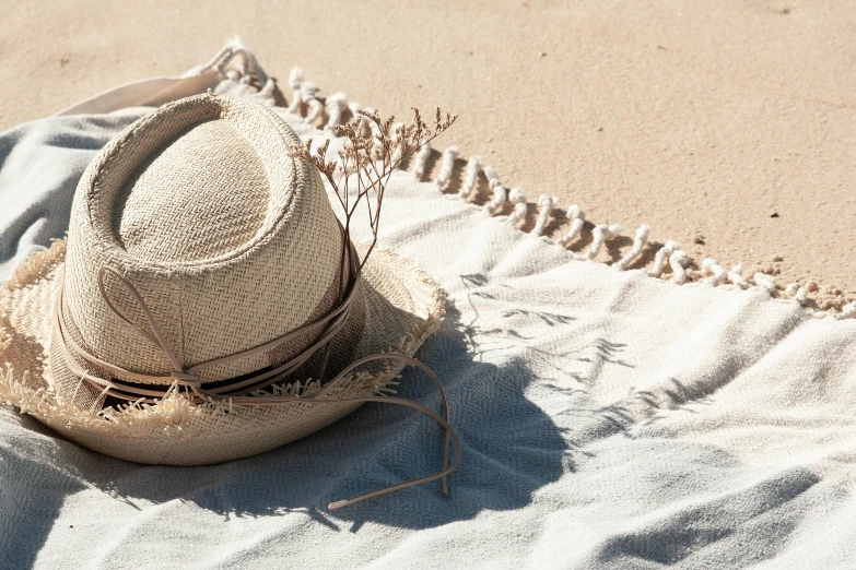 a hat sitting on top of a blanket on a beach, a still life, by Nina Hamnett, unsplash, silver，ivory, light tan, bright sun bleached ground, handcrafted