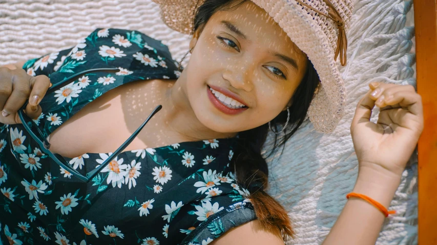 a woman laying in a hammock with a hat on, inspired by Ruth Jên, unsplash, hurufiyya, dressed in a flower dress, south east asian with round face, teenager girl, detailed smile