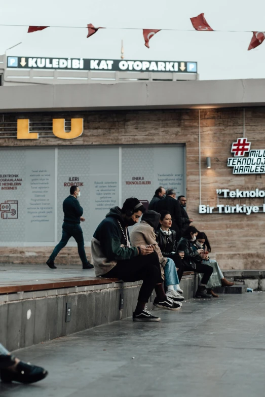 a group of people sitting on a bench in front of a building, a poster, trending on pexels, hurufiyya, turkey, ui and ux, terminal, storefront