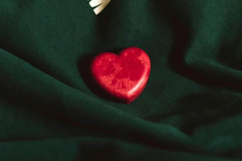 a red heart sitting on top of a green cloth, made of marble, ornate dark green clothing, shot with sony alpha, full frame image