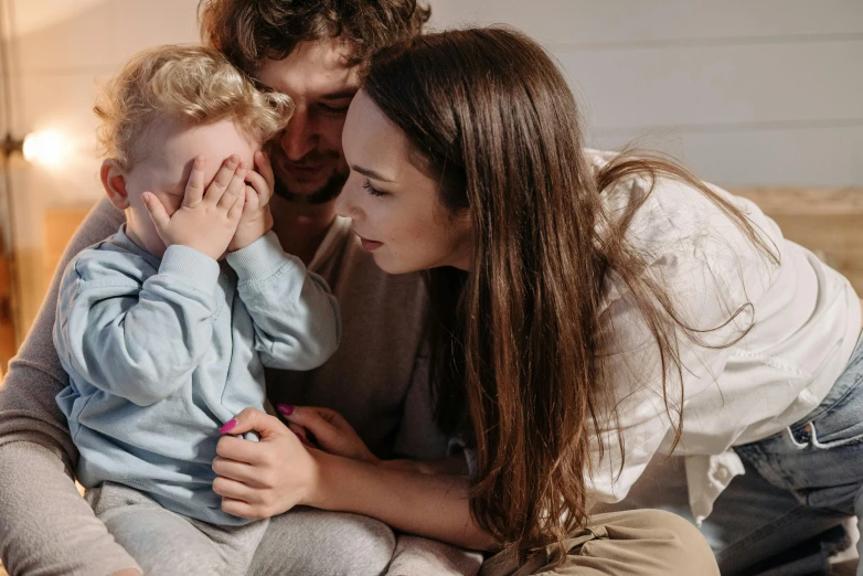 a man sitting on top of a bed next to a woman holding a baby, pexels contest winner, incoherents, noticeable tear on the cheek, little boy, profile image, looking exhausted