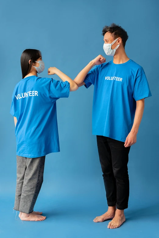 a man putting a mask on a woman's face, a colorized photo, pexels contest winner, happening, blue tight tshirt, colorful uniforms, reaching out to each other, blue wall