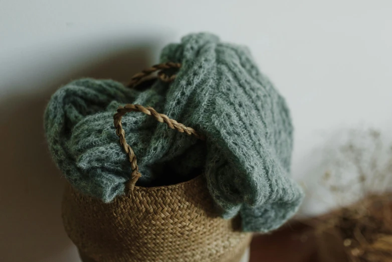 a knitted bag sitting on top of a wooden table, trending on pexels, hurufiyya, pastel green, grey, hazy, cozy wallpaper