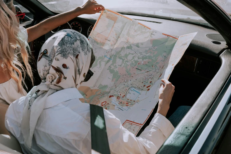 a woman sitting in a car looking at a map, by Matija Jama, trending on unsplash, visual art, white hijab, foil, nautical maps, wearing a scarf