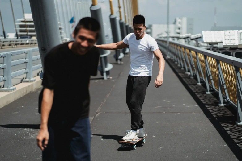 a man riding a skateboard across a bridge, pexels contest winner, happening, zeen chin and terada katsuya, wearing pants and a t-shirt, wearing casual clothing, scratches on photo