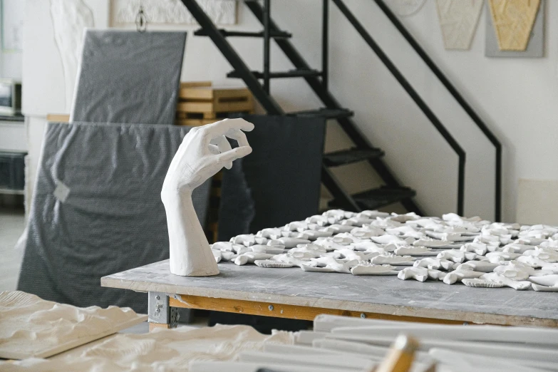 a sculpture sitting on top of a wooden table, a marble sculpture, unsplash, new sculpture, raised hand, stood in a factory, white ceramic shapes, plated arm