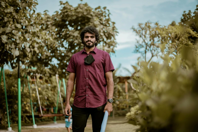 a man in a red shirt holding a skateboard, by Max Dauthendey, pexels contest winner, standing in a botanical garden, jayison devadas, avatar image, looking towards the camera