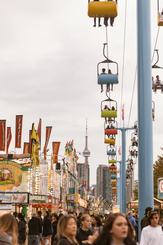a crowd of people walking down a street next to tall buildings, by Julia Pishtar, trending on unsplash, digger land amusement park, toronto, swings, west world show