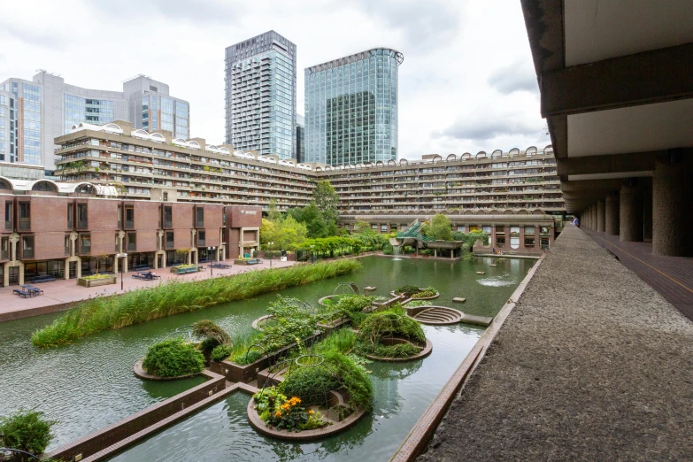 a river running through a city next to tall buildings, brutalism, with a fishpond and courtyard, carrington, gardens and fountains, exterior photo