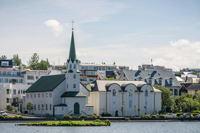 a large white church sitting next to a body of water, by Þórarinn B. Þorláksson, pexels contest winner, hurufiyya, modernist buildings, neighborhood, asymmetrical spires, to