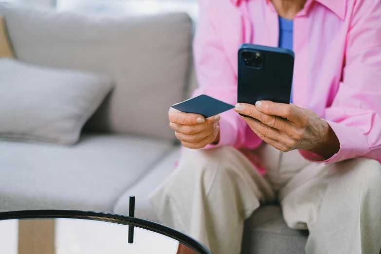 a man sitting on a couch holding a smart phone, a picture, by Carey Morris, trending on pexels, happening, elderly woman, pink and blue colour, a person standing in front of a, healthcare