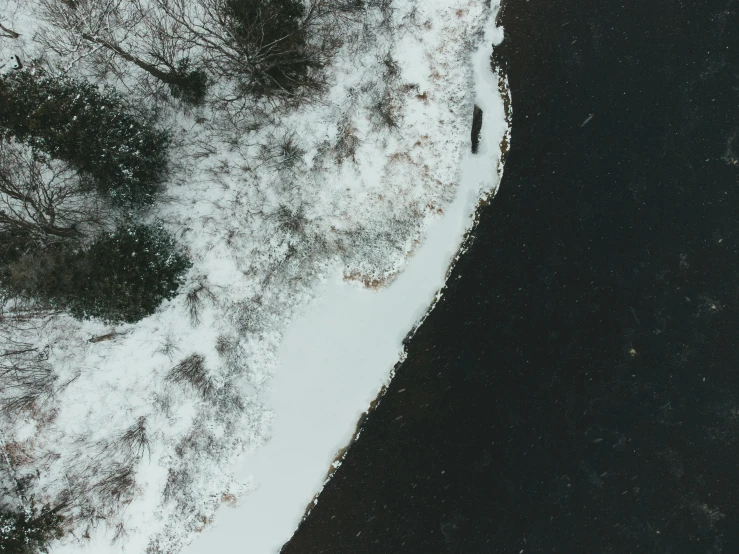 a body of water surrounded by trees covered in snow, by Emma Andijewska, pexels contest winner, land art, some of the blacktop is showing, white on black, looking down at you, half and half